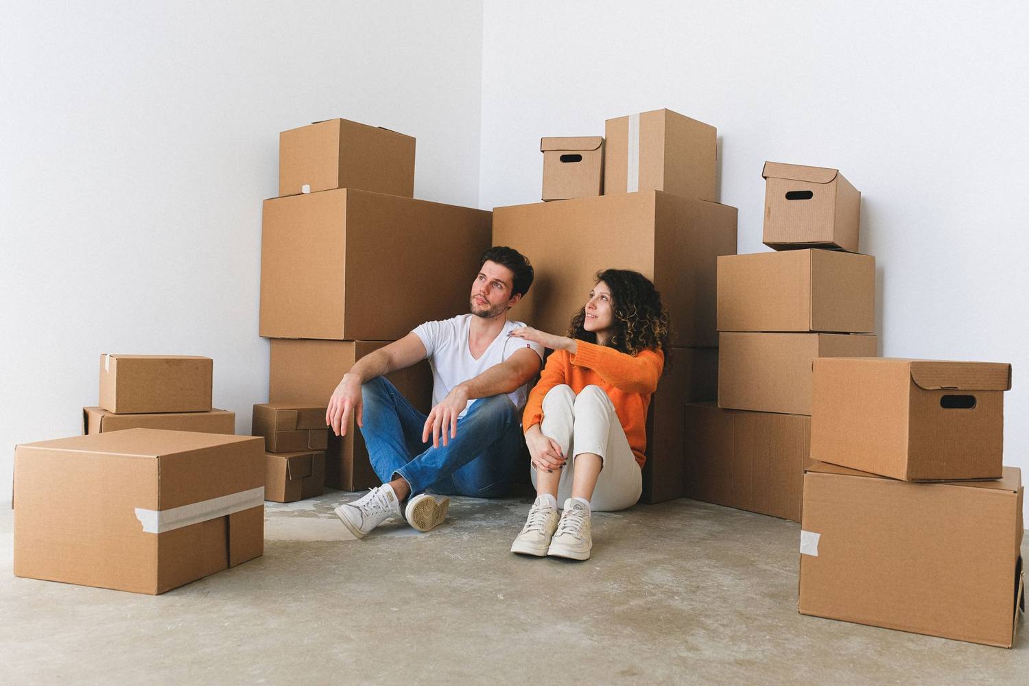 Jeune couple assis parmi des cartons après avoir emménagé dans une nouvelle maison, profitant d'un moment ensemble.